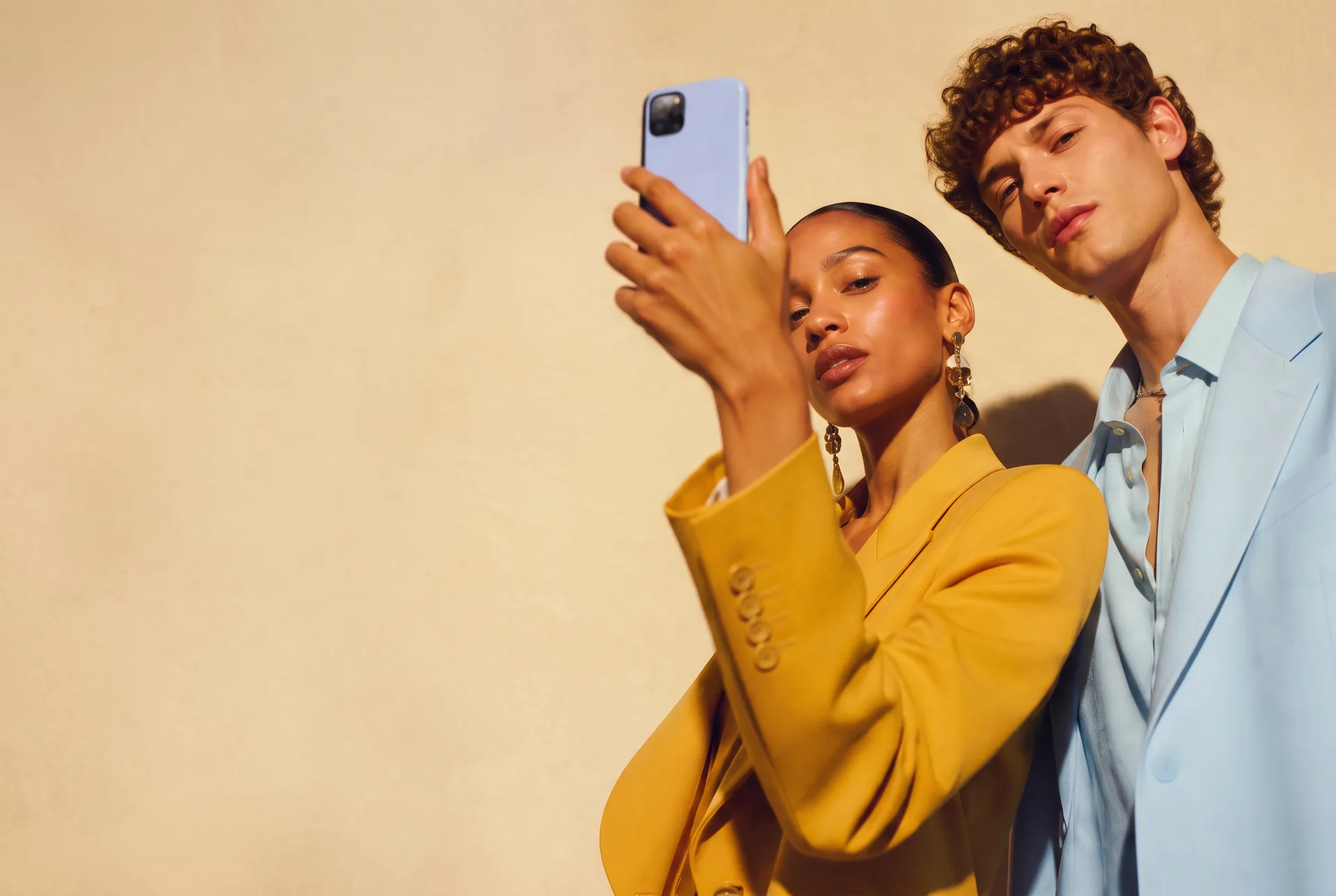 Two creative professionals in yellow and blue holding up a phone
